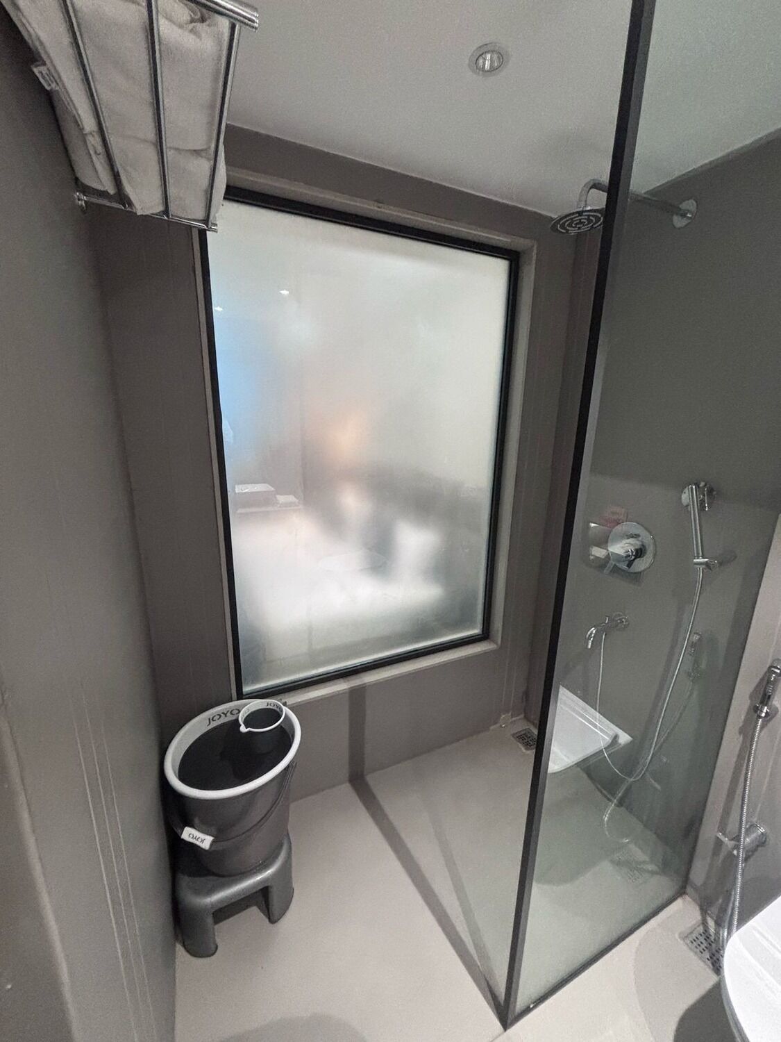 Un baño moderno con cabina de ducha de vidrio, un inodoro con cubo de basura y una ventana con vidrio esmerilado.