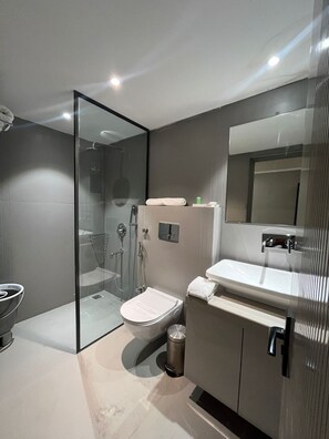 Un baño moderno con ducha de vidrio, inodoro, lavamanos y espejo.