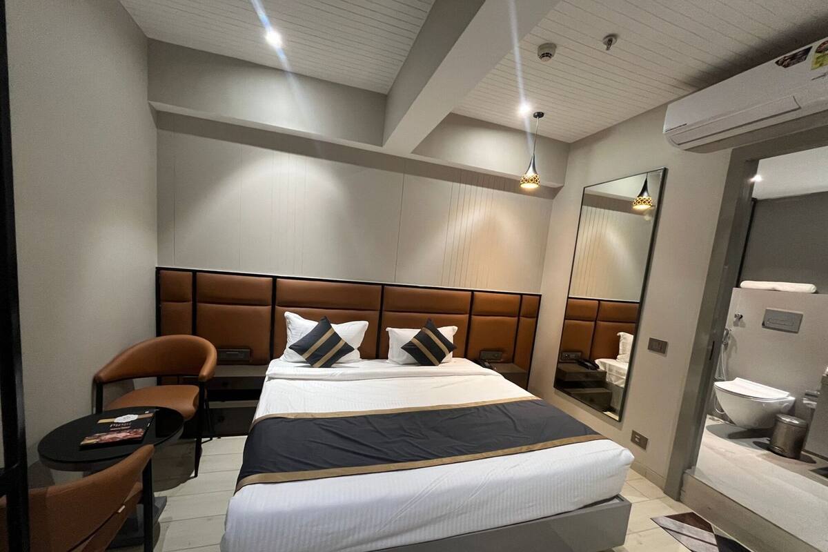A modern hotel room with a large bed, a seating area with a chair, a small table, and a mirror.