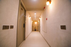 A narrow hallway with a light-colored floor, a door on the left, and a wall-mounted light fixture on the right.