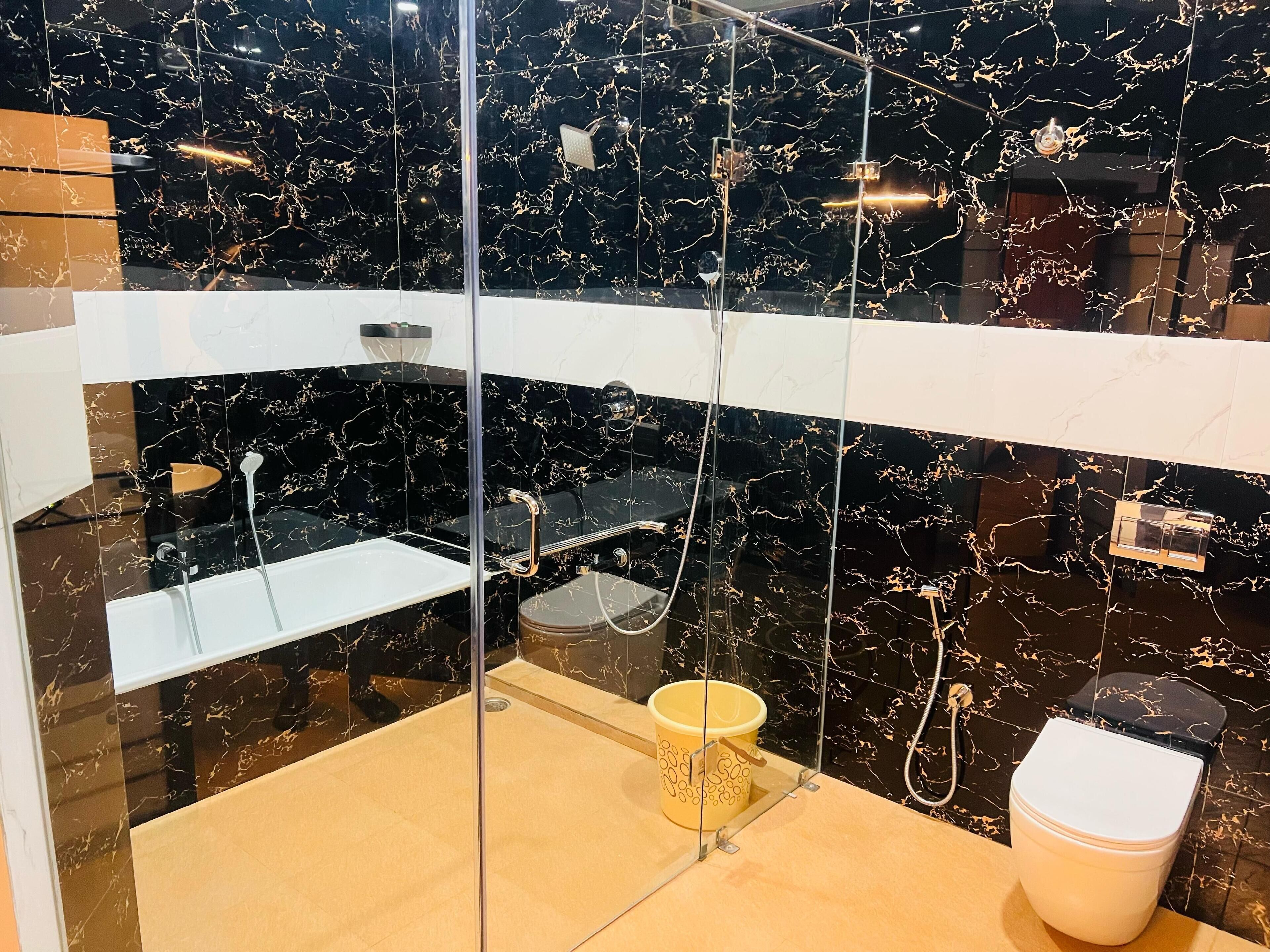 A modern bathroom with a glass-enclosed shower, marble walls, and a toilet.