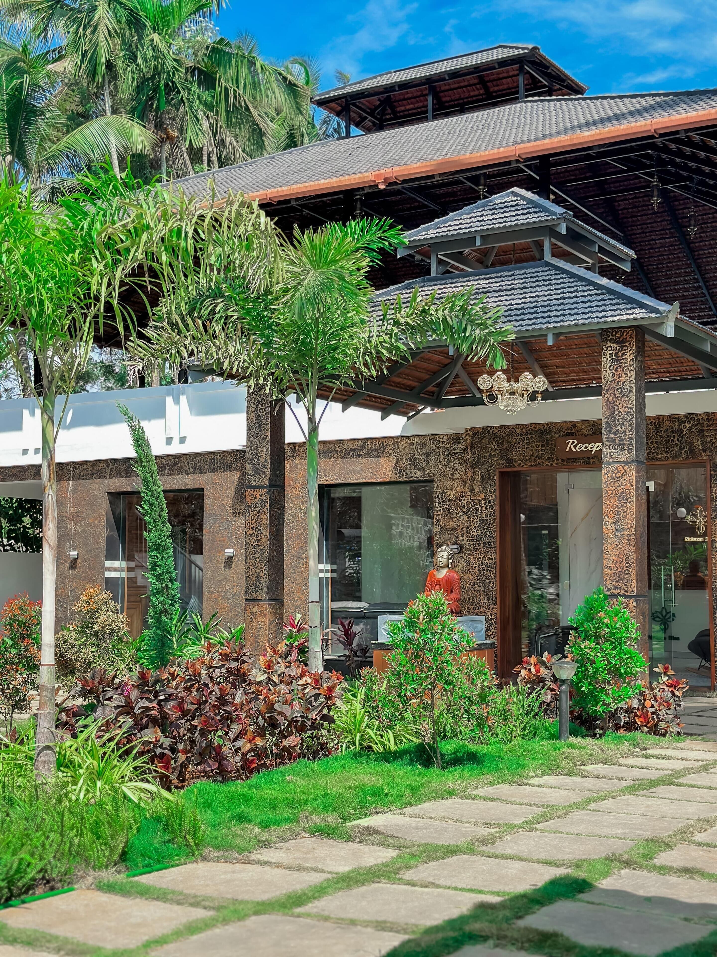 Ein Hotel mit Eingangsbereich, einer Rezeption, Palmen und einer Buddha-Statue.