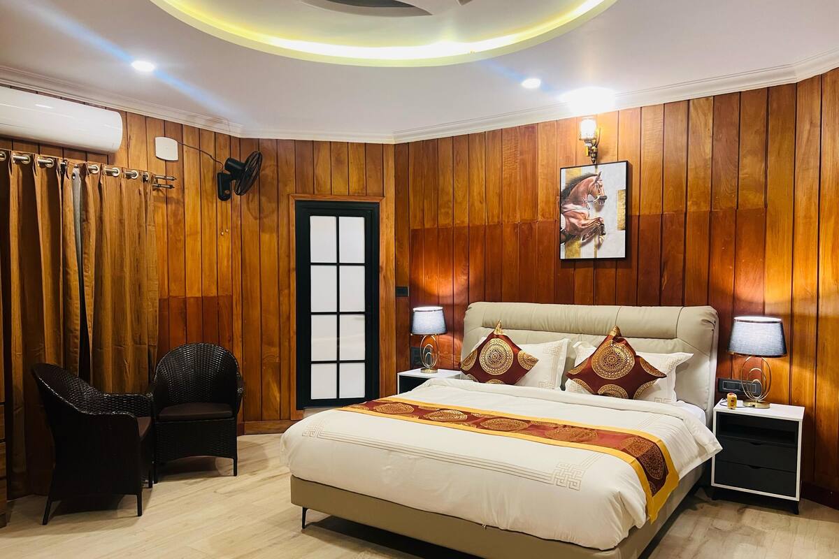 Un dormitorio con cama, dos mesitas de noche, una silla, una puerta y paneles de madera en las paredes.