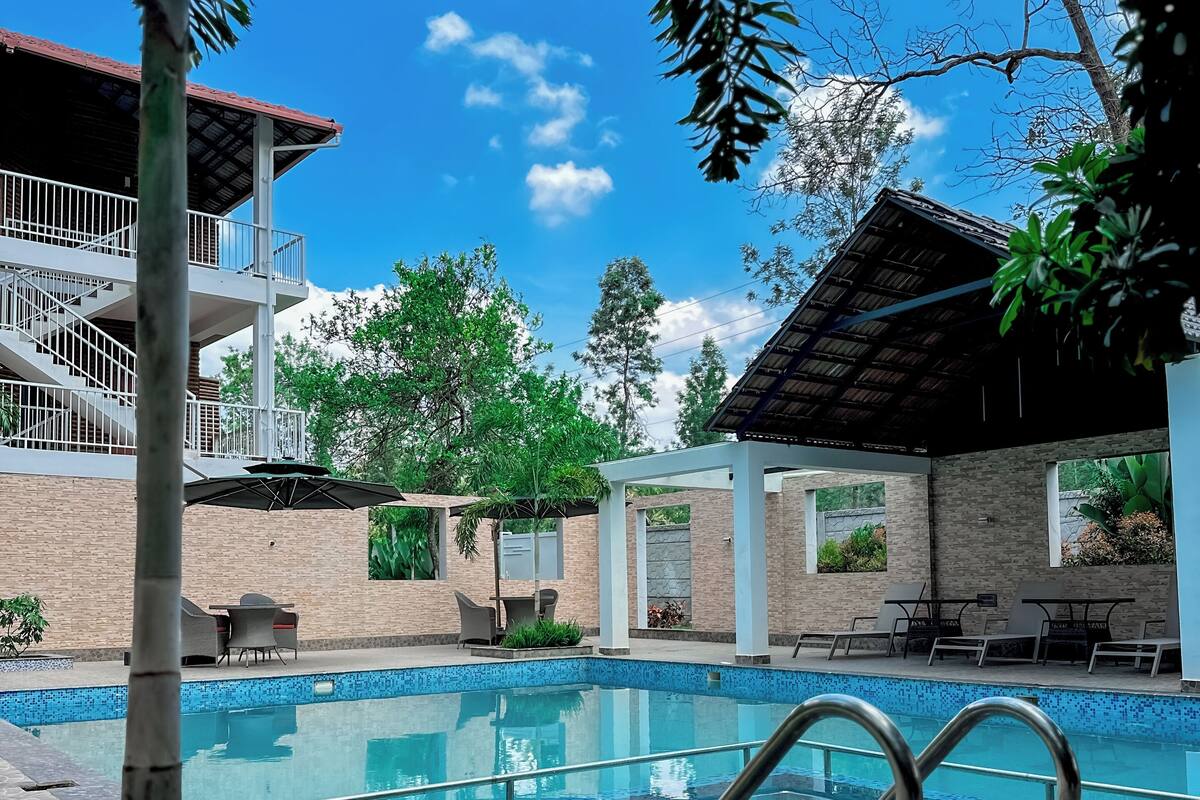 Una piscina con borde de baldosas, rodeada de sillas de descanso y un área de estar techada.