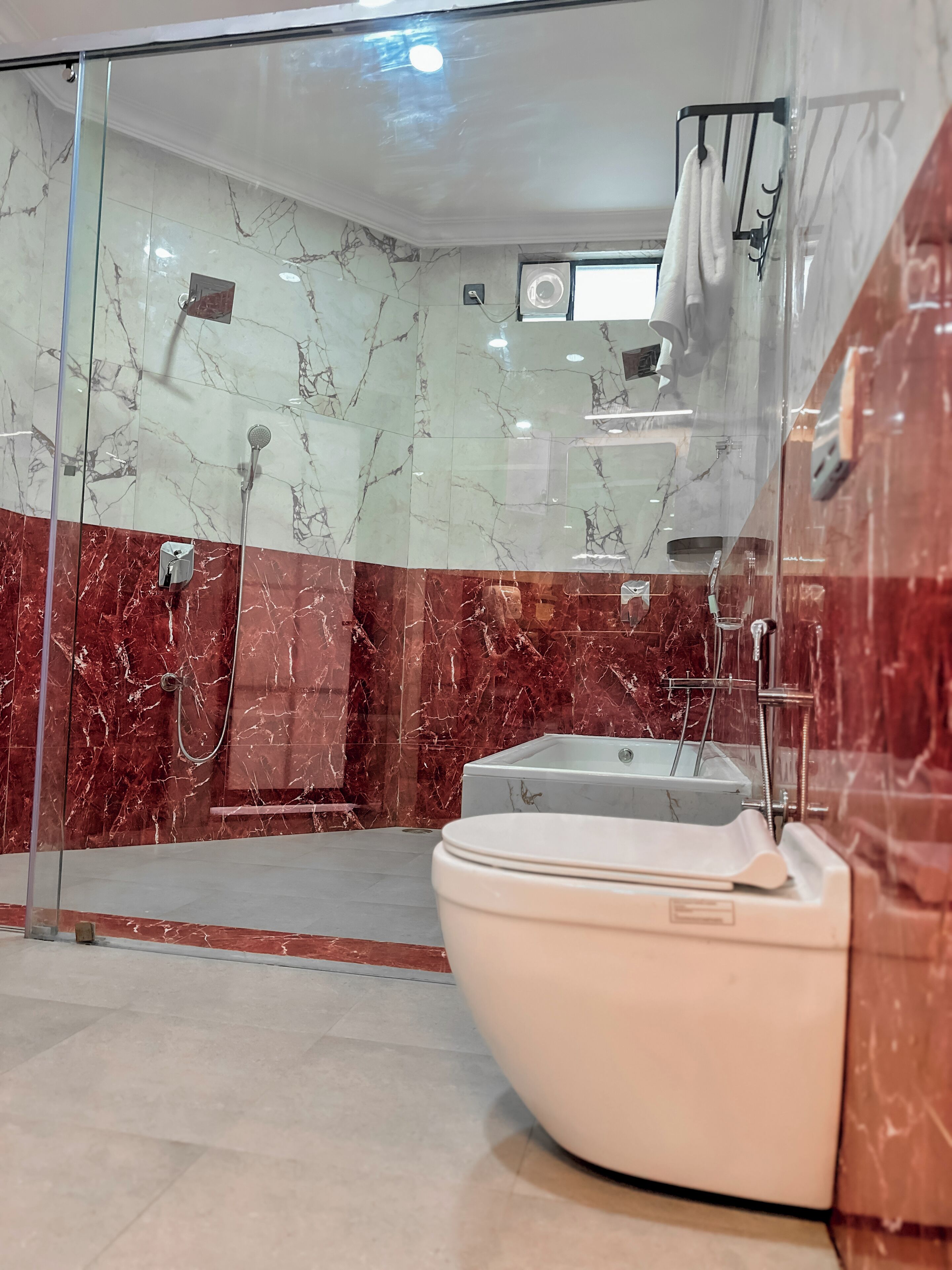 A modern bathroom with a glass-enclosed shower, a white toilet, and marble walls.