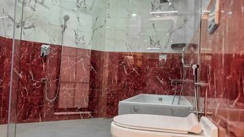 A modern bathroom with a glass-enclosed shower, a white toilet, and marble walls.