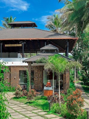 A traditional building with a tiled roof, a sign indicating a restaurant, and a Buddha statue in the garden. - Natures Bliss Resort Coorg (Somvarpet)