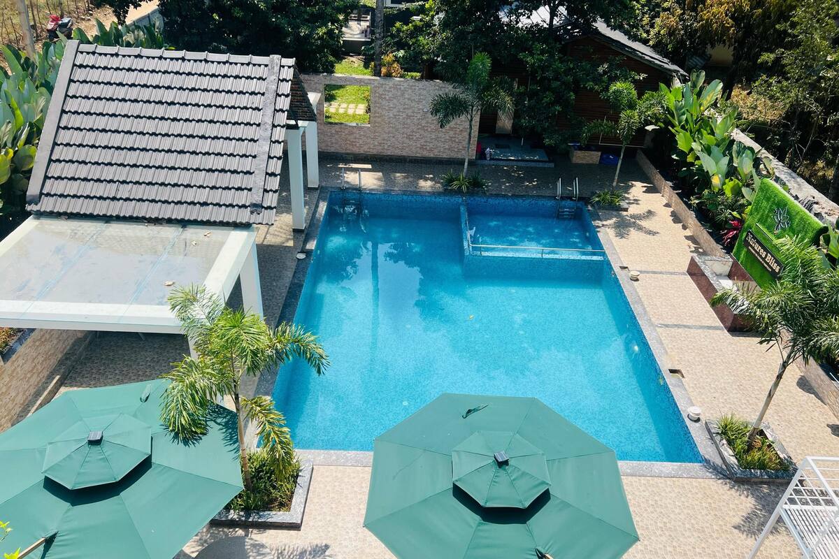 Una piscina con dos sombrillas, una zona de estar techada y un pequeño jardín.