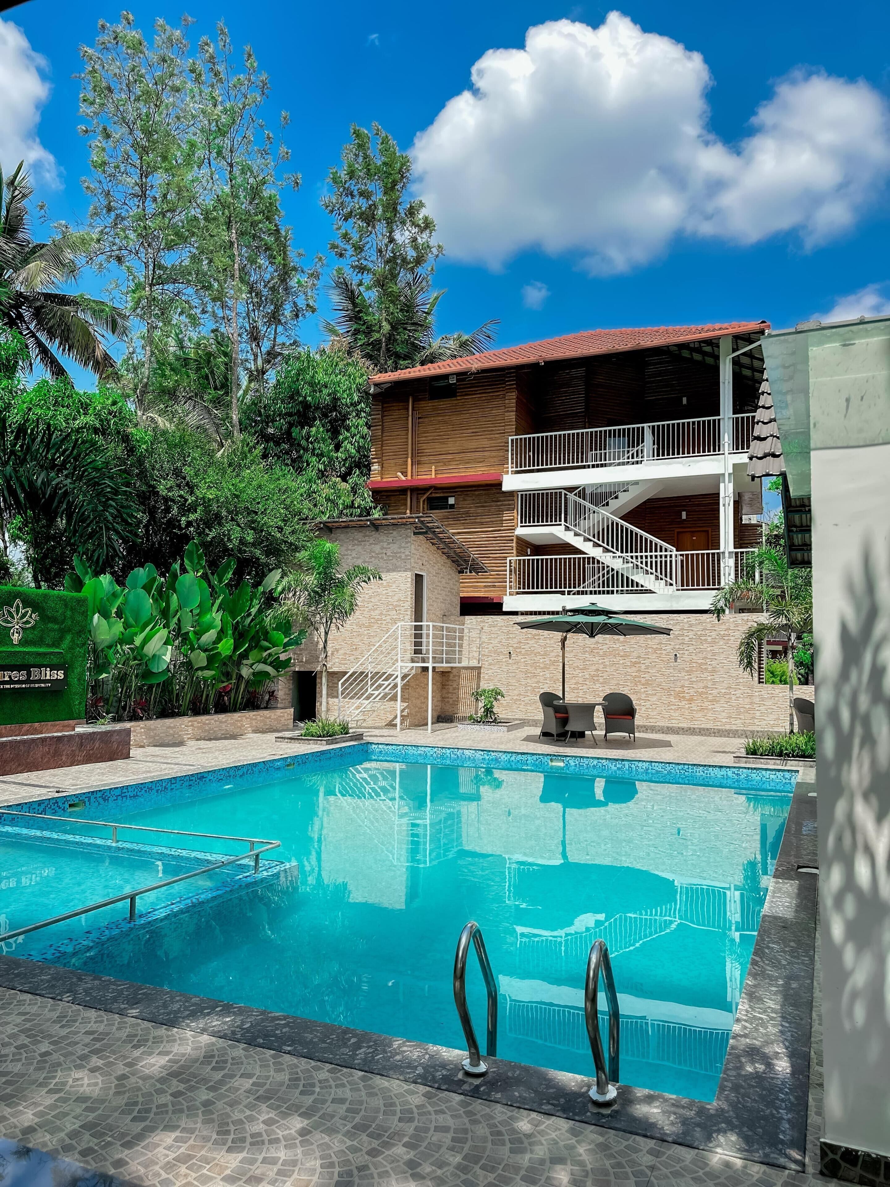 A swimming pool with a wooden deck and a two-story building with a balcony in the background.