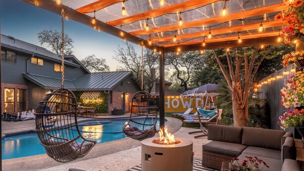 An outdoor pool area with a fire pit, hanging chairs, and a covered seating area with string lights.