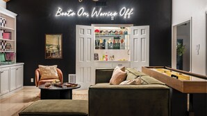 A modern living room with a foosball table, a comfortable sofa, a bookshelf, and a neon sign on the wall.
