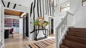 A modern interior with a staircase, a checkered wall, and a console table with a mirror and plants.