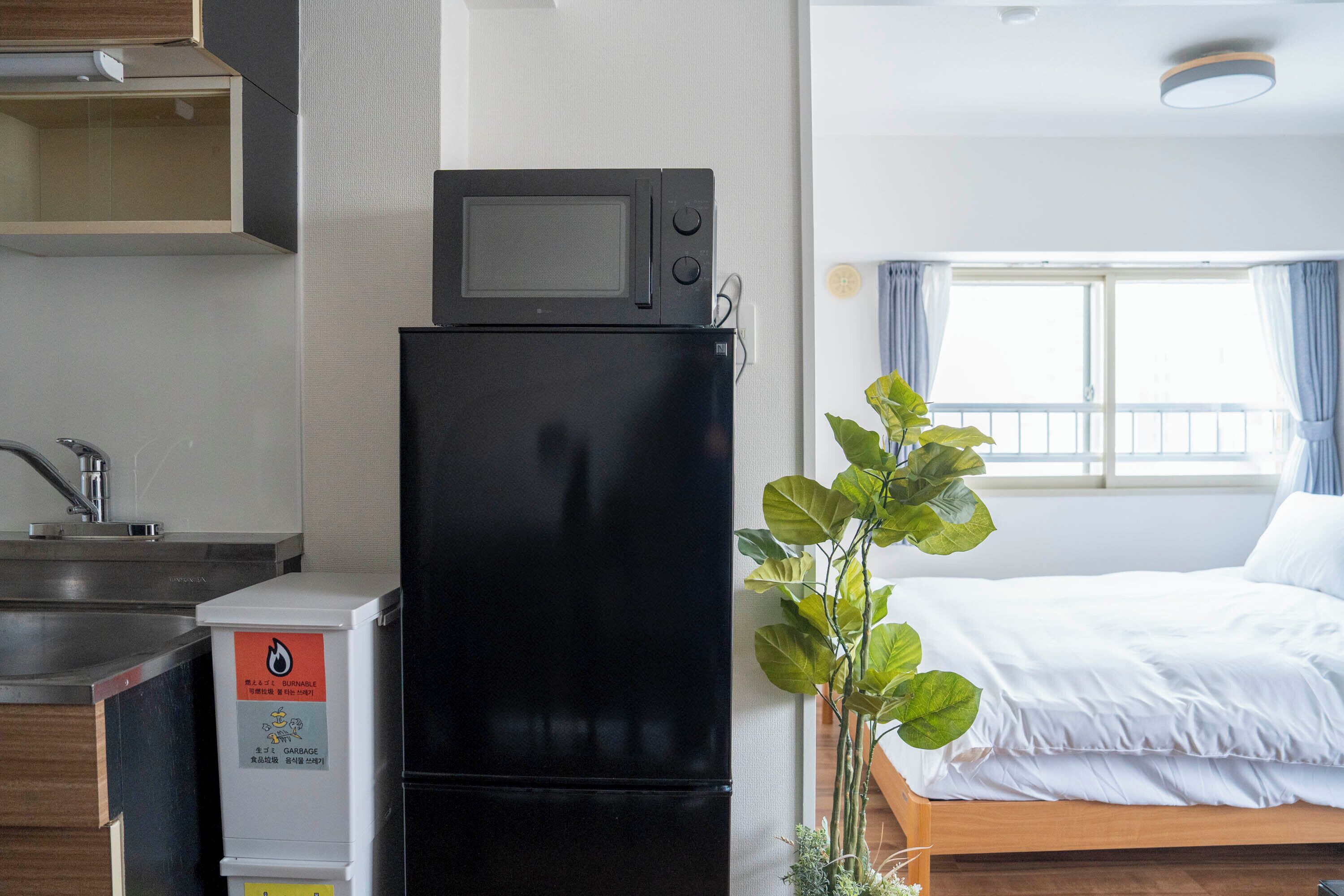 Cocina compacta equipada con microondas y refrigerador, un lavamanos y una cama con vista al exterior.