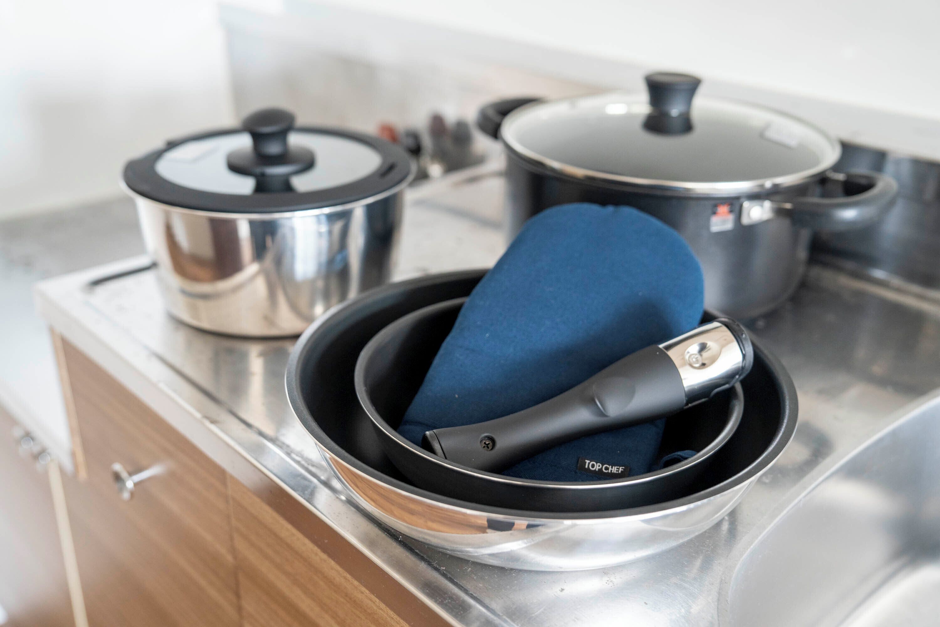 A kitchen with stainless steel appliances, including a pot with a lid and a pan with a blue handle.