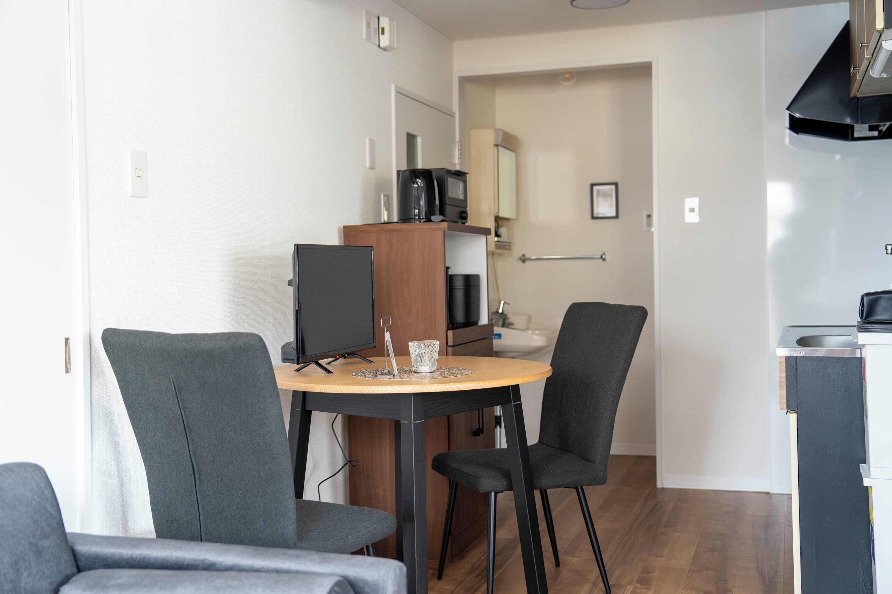 A compact living space with a dining area featuring a round table and four chairs, a kitchenette with a microwave, and a small sink.