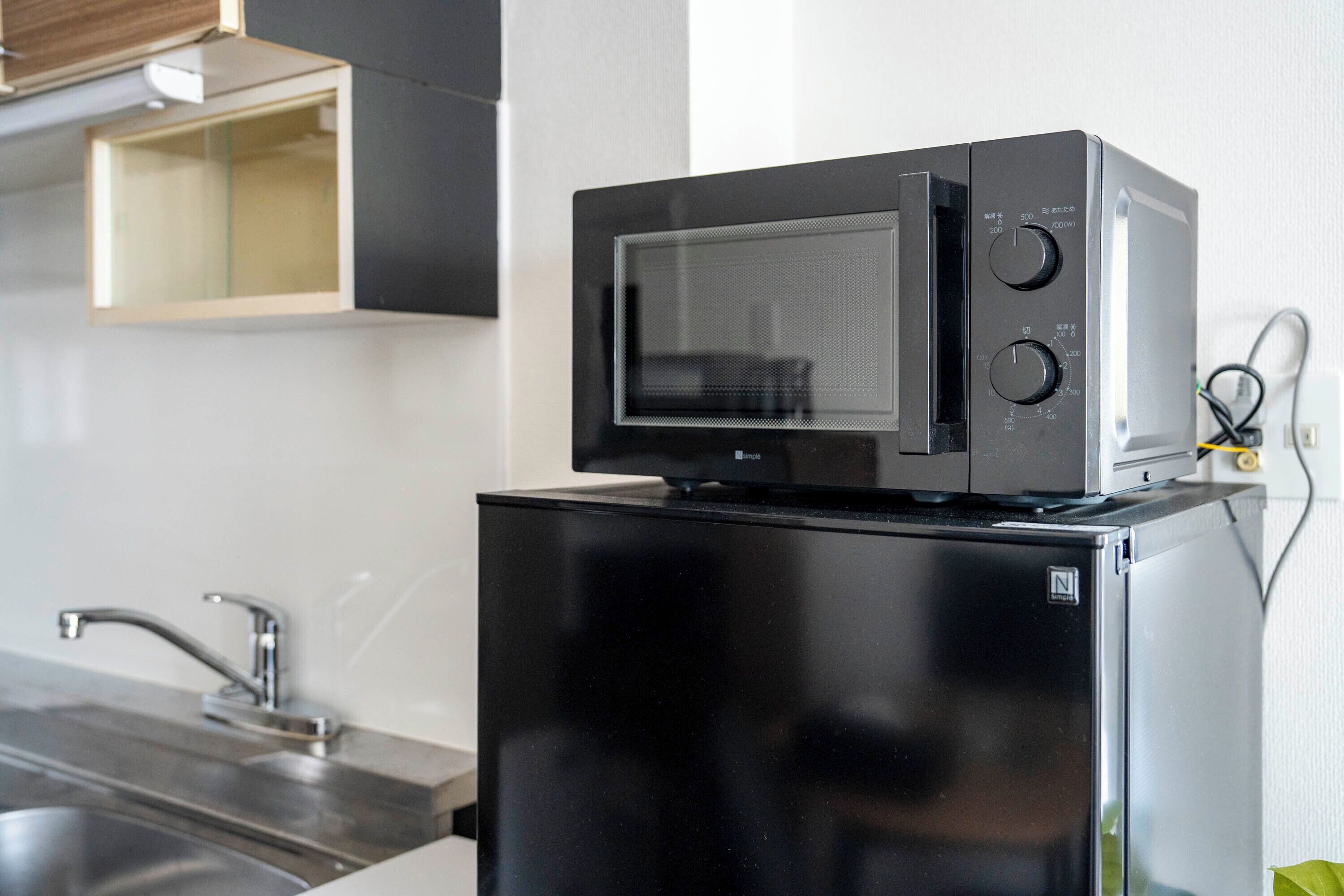 Una cocina compacta con un refrigerador negro, un microondas encima y un lavamanos de acero inoxidable.