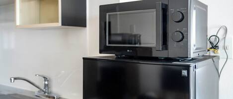 Una cocina compacta con un refrigerador negro, un microondas encima y un lavamanos de acero inoxidable.