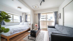 A modern hotel room with a bed, a sofa, a small table, and a large window with curtains. - SPACE 701 (Sapporo)