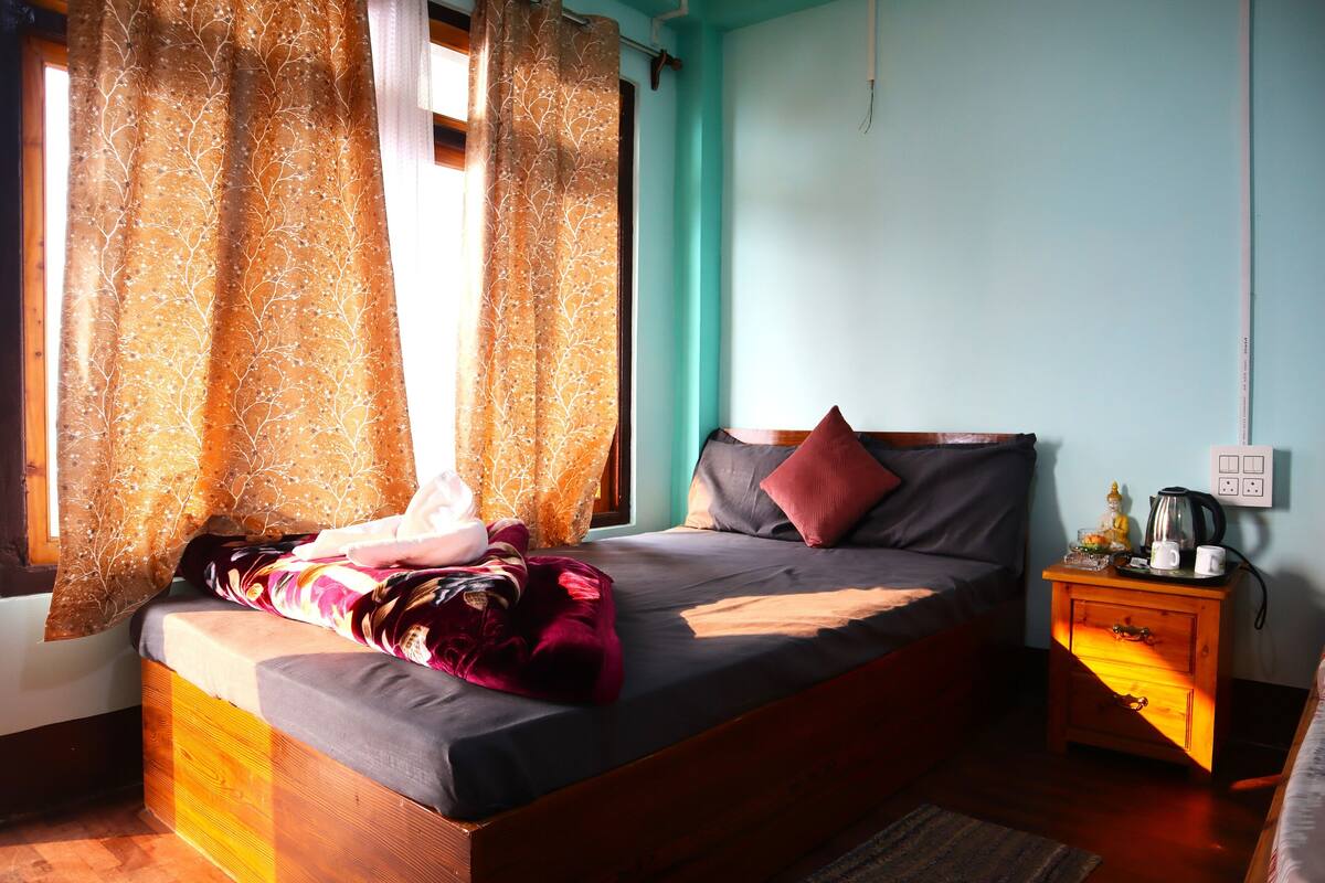 A bedroom with a bed, a nightstand, a window with curtains, and a wall socket.