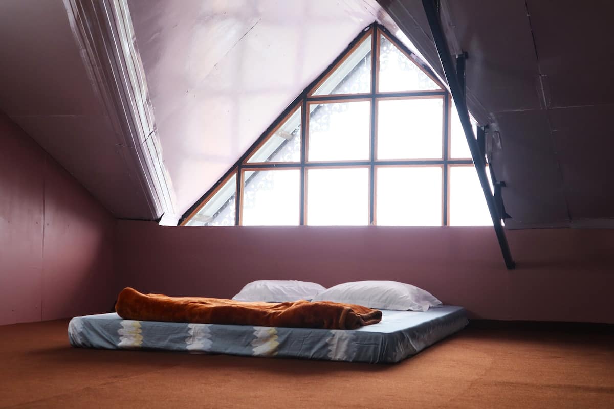 A small, dimly lit room with a single bed, a window, and a sloped ceiling.