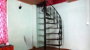 Une pièce avec un escalier en colimaçon, une armoire en bois et un rideau à motifs roses.