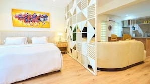 A hotel room with a bed, a sofa, a decorative partition, a painting, and a kitchenette. - Blossom Service Apartment  (Lagos)