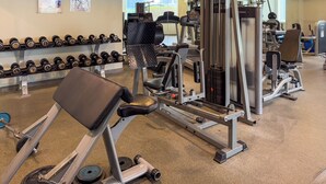 Een sportschool met diverse fitnessapparaten, waaronder gewichten, een bank en krachttoestellen.