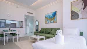 Een moderne hotelkamer met een bed, een groene bank, een eethoek met tafel en stoelen, en een keuken op de achtergrond.