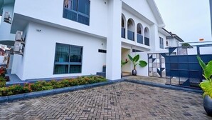Una casa moderna de dos pisos con un patio empedrado, ventanas grandes y entrada protegida por una reja.