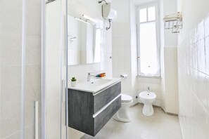 Une salle de bain moderne avec une douche à parois de verre, un meuble-lavabo en bois foncé, des toilettes blanches et un bidet.