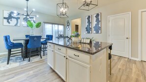 A modern kitchen with a central island, white cabinetry, and blue chairs. - Entire Home-Beautiful 4BR, 3.5BA Retreat in Ankeny, Iowa 2 King Beds, Fenced, AC (Ankeny)