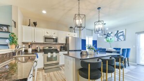 A modern kitchen with white cabinets, stainless steel appliances, and a central island with bar stools. - Entire Home-Beautiful 4BR, 3.5BA Retreat in Ankeny, Iowa 2 King Beds, Fenced, AC (Ankeny)