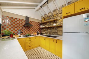 Une cuisine avec des armoires jaunes, un mur en pierre, une hotte noire et un réfrigérateur blanc.