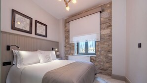 Una camera da letto con un letto, un muro in pietra, una finestra con persiana e due opere d'arte incorniciate appese alla parete.