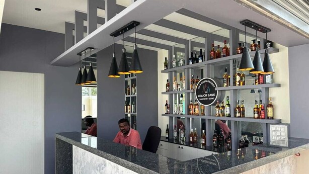 Un espace bar doté d’un comptoir en marbre, de plusieurs étagères remplies de bouteilles d’alcool et de luminaires suspendus.