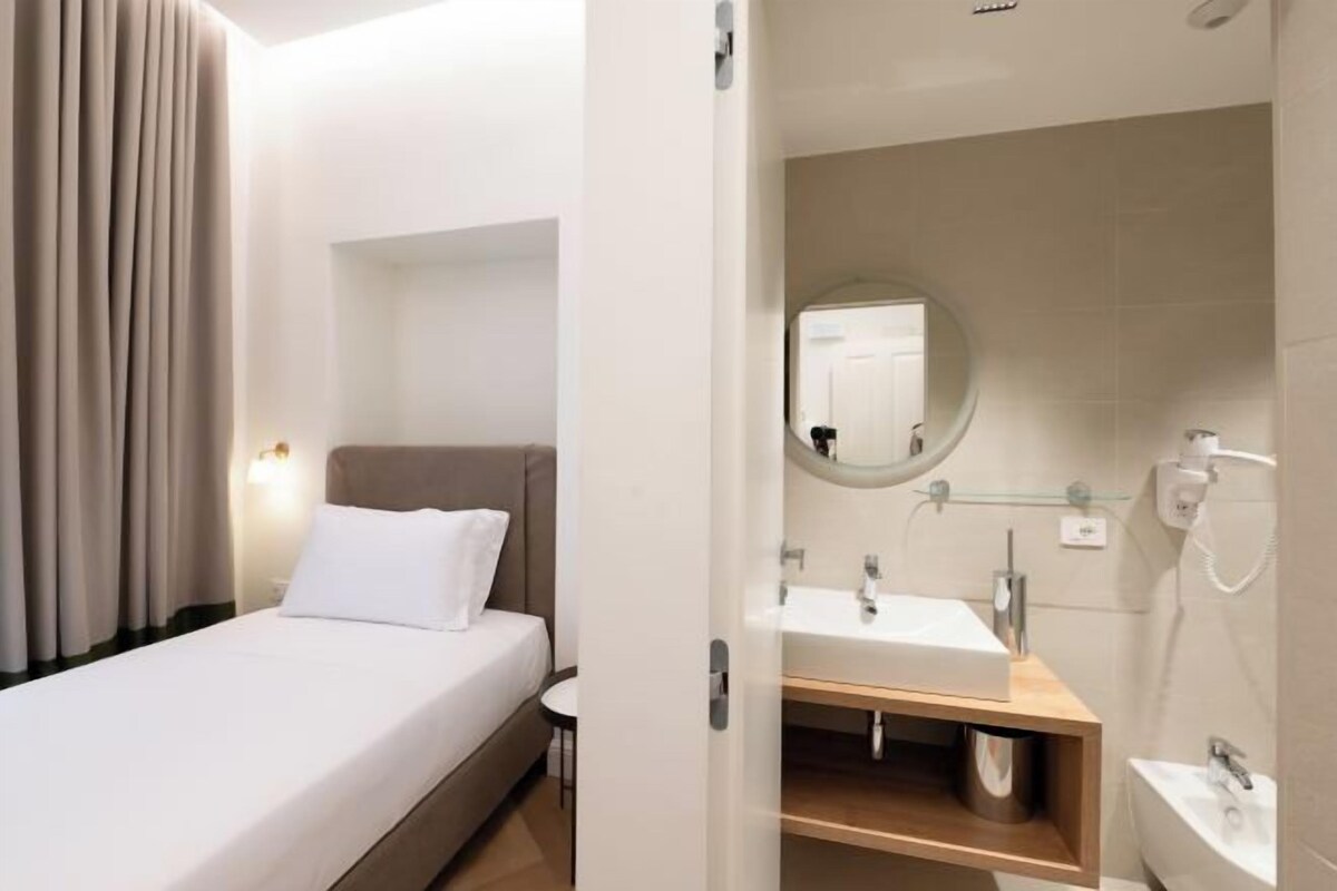Een hotelkamer met een bed, nachtkastje, spiegel, wastafel en douche.