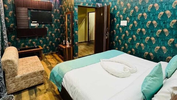 A bedroom with a bed, a chair, a TV, and a wardrobe. - Hotel Rajveer Inn (Varanasi)