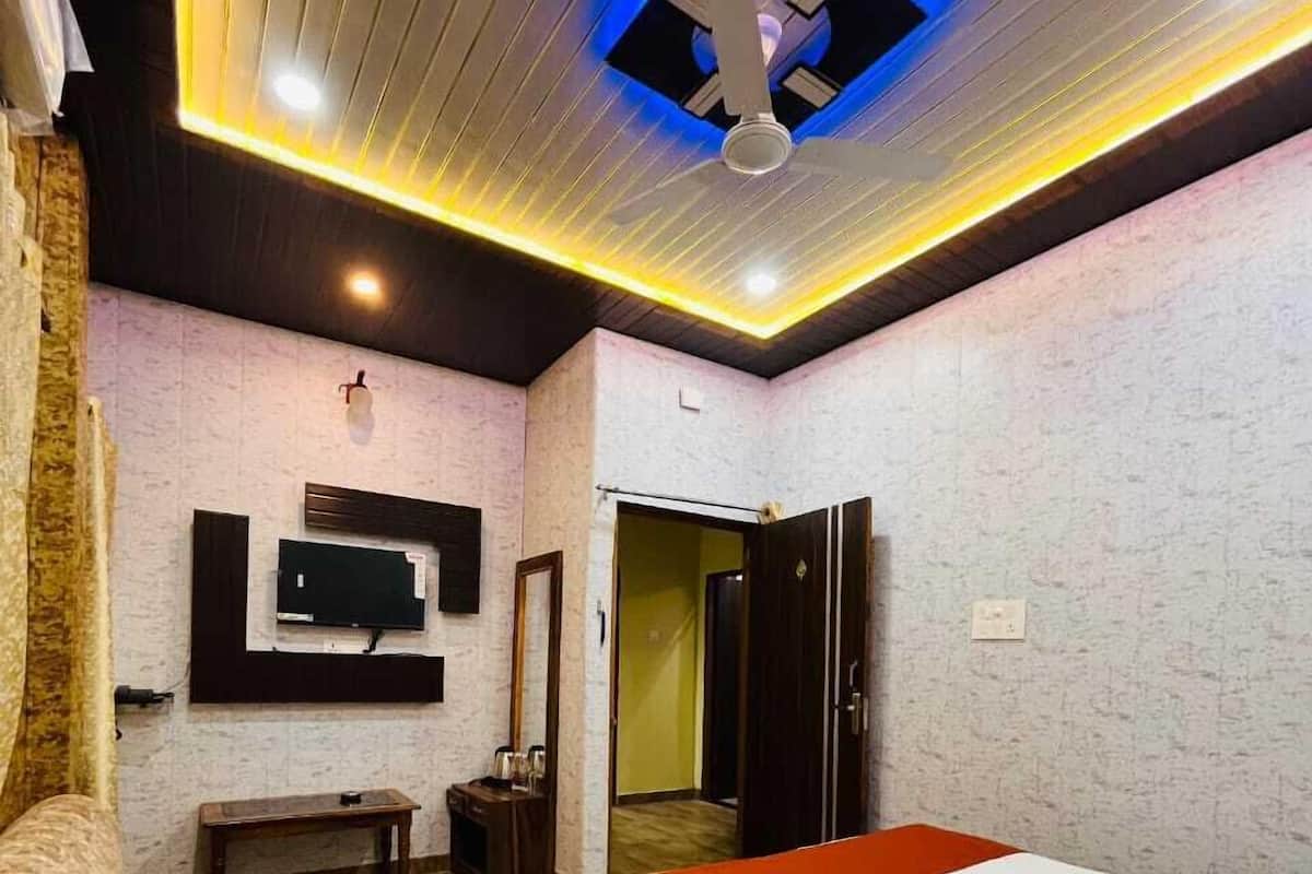 A hotel room with a bed, a TV mounted on the wall, a wooden floor, and a ceiling with recessed lighting.