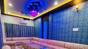 A room with a sofa area, tables, patterned walls, and a chandelier. - Hotel Rajveer Inn (Varanasi)