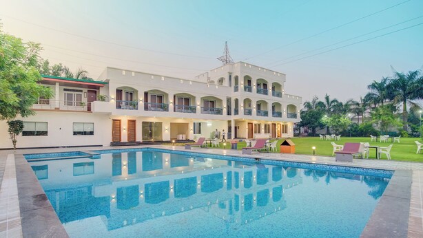 A hotel with a swimming pool, outdoor seating, and a well-maintained lawn. - Bliss Resort (Rishikesh)