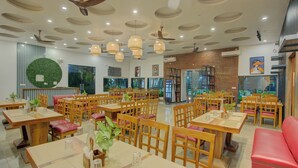 A spacious restaurant with wooden tables and chairs, ceiling fans, and hanging light fixtures. - Bliss Resort (Rishikesh)