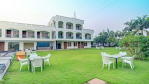 A two-story building with multiple balconies, a grassy courtyard with outdoor seating, and a clear sky. - Bliss Resort (Rishikesh)