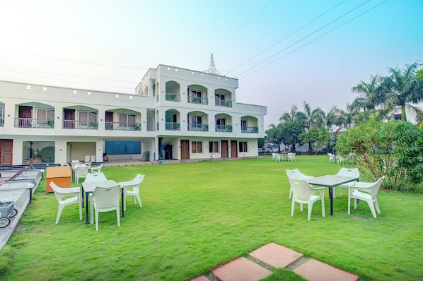 A two-story building with multiple balconies, a grassy courtyard with outdoor seating, and a clear sky.