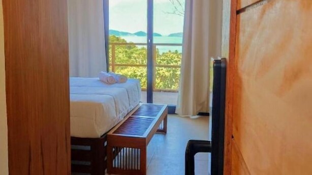 Une chambre avec un lit, un banc et une vue sur l’extérieur.