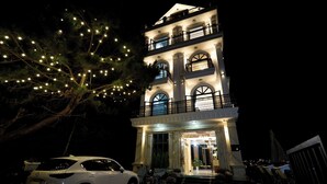 A multi-story hotel with a grand entrance, a balcony on the upper floor, and a white car parked in front. - Lotus Hotel Da Lat (Xuan Truong - Da Lat)