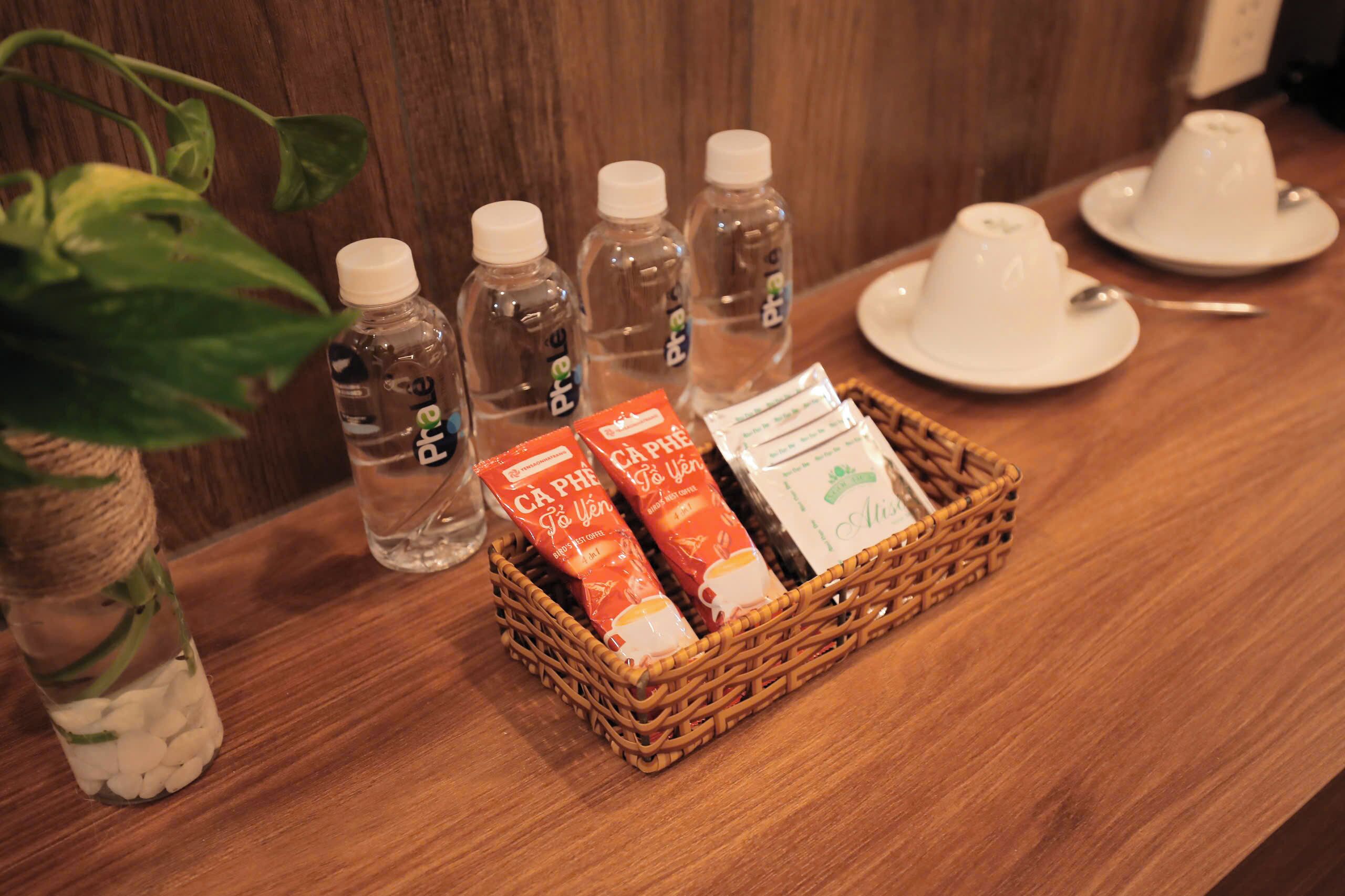 A wooden table with a wicker basket containing two packets of coffee, a bottle of water, and a white cup.