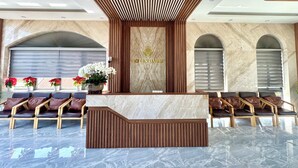 A reception area with a marble reception desk, wooden paneling, and a logo. There are seating areas with leather chairs and a potted plant. - Lotus Hotel Da Lat (Xuan Truong - Da Lat)