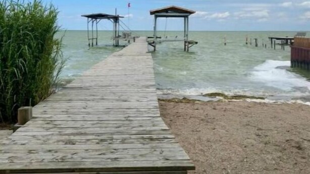 Une jetée en bois menant à une plage où se trouvent deux constructions abritées.