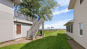 Il s’agit d’une propriété résidentielle dotée d’une pelouse bien entretenue, d’un escalier en bois menant à une terrasse, et offrant une vue sur l’océan en arrière-plan.