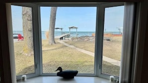 Une baie vitrée donnant sur une plage, une terrasse en bois et une figurine de canard posée sur le rebord de la fenêtre.